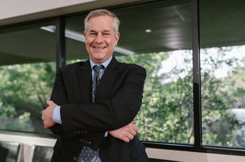 Senior manager con traje sonriendo y brazos cruzados en una oficina moderna